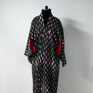 May include: A long, patterned kimono in shades of black, green, and white, displayed on a mannequin. The kimono features a diamond pattern and red accents on the sleeves. The garment is made of a soft, flowing fabric.