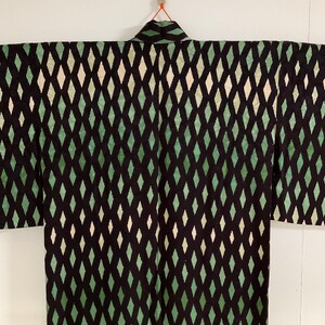 May include: A black kimono with a repeating diamond pattern in shades of green and off-white. The kimono is hanging against a white background, showcasing the full garment and its design.