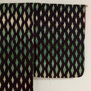 May include: A dark kimono with a repeating diamond pattern in shades of green and off-white against a black background. The garment is hanging, showcasing the full length and sleeve details. The interior lining is a reddish color.