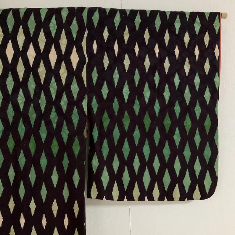 May include: A dark kimono with a repeating diamond pattern in shades of green and off-white against a black background. The garment is hanging, showcasing the full length and sleeve details. The interior lining is a reddish color.