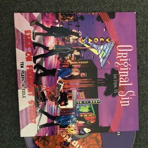 May include: A purple CD with the text "Original Sin LV" and a red graphic of a brain with the text "CaiRip" on it. The CD is in a clear plastic case with a purple and white cover that says "Original Sin" and "Las Vegas, NV". The cover also has a picture of a street scene with people walking on a crosswalk.