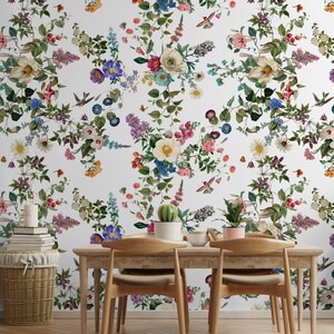 May include: A white wall with a floral wallpaper featuring a repeating pattern of colorful flowers, leaves, and hummingbirds. The wallpaper is in a dining room with a wooden table and chairs.
