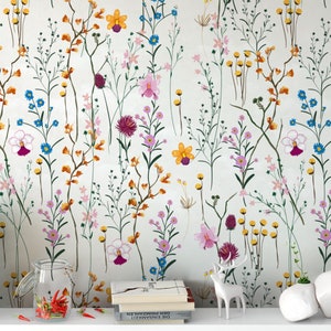 Könnte beinhalten: Ein weißer Hintergrund mit einem floralen Muster mit rosa, gelben, orangefarbenen, blauen und violetten Blumen. Die Blumen sind in einem zufälligen Muster angeordnet und von grünen Blättern umgeben.