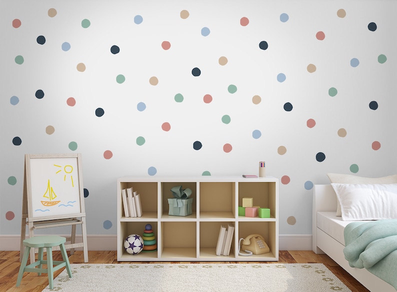 May include: A white wall with a colorful polka dot pattern. The wall is decorated with blue, green, pink, and brown dots. There is a white bookshelf with a few items on the shelves, a white easel with a drawing of a boat and sun, and a white bed with a light blue blanket.