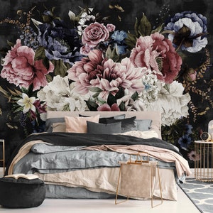 May include: A bedroom with a black and white floral wallpaper featuring large pink, white, and blue flowers. The bed has a black throw blanket, a light blue duvet, and pink and gray pillows. A gold metal side table with a glass cloche sits in the corner.
