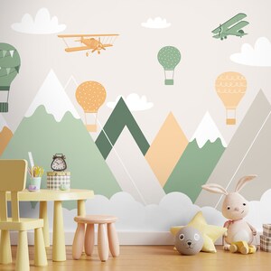 May include: A children's playroom with a light gray wall featuring a whimsical mural of mountains, clouds, hot air balloons, and airplanes. A yellow child's chair and table are in the foreground, along with a stuffed bunny and other toys.