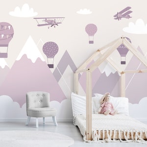 May include: A light purple and white children's room with a wooden bed frame, a white armchair, and a wall mural featuring mountains, clouds, hot air balloons, and airplanes.