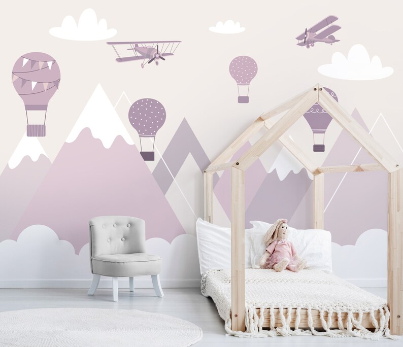 May include: A light purple and white children's room with a wooden bed frame, a white armchair, and a wall mural featuring mountains, clouds, hot air balloons, and airplanes.