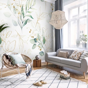 May include: A living room interior with a light gray sofa, a white wicker chair, and a white rug with a black diamond pattern. The wall is decorated with a wallpaper featuring a watercolor design of green leaves and gold branches.
