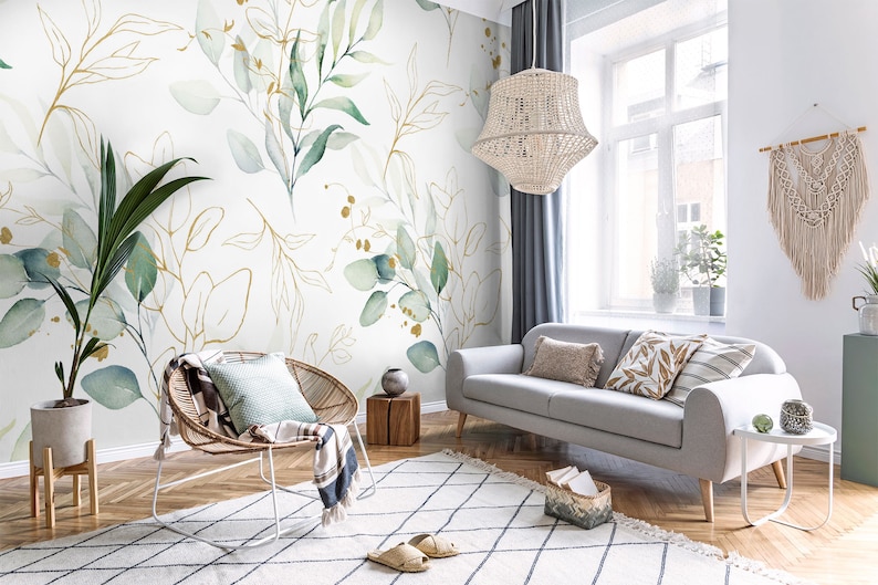 May include: A living room interior with a light gray sofa, a white wicker chair, and a white rug with a black diamond pattern. The wall is decorated with a wallpaper featuring a watercolor design of green leaves and gold branches.