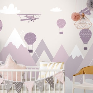 May include: A nursery room with a white crib and a purple, white, and gray mountain themed mural with hot air balloons and an airplane. The crib has a pink and gray garland and a pink star-shaped pillow.