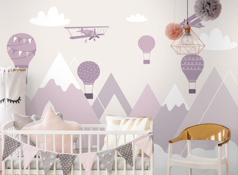 May include: A nursery room with a white crib and a purple, white, and gray mountain themed mural with hot air balloons and an airplane. The crib has a pink and gray garland and a pink star-shaped pillow.