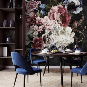 May include: A round wooden dining table with four blue velvet chairs. The table is set with plates, glasses, and silverware. The background is a dark floral wallpaper with large pink and white flowers.