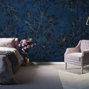 May include: A bedroom interior with a bed, a chair, and a floor lamp. The walls are covered in a blue wallpaper with a gold floral pattern. The bed has a pink headboard and a gray blanket. The chair is upholstered in pink fabric. The floor lamp has a gold base and a white shade.
