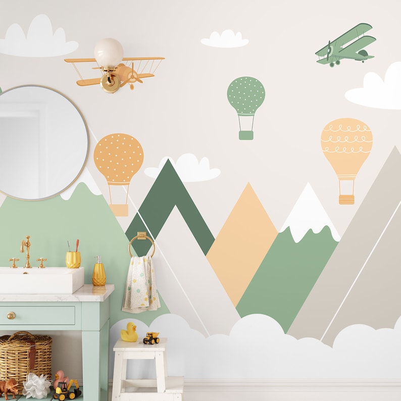 May include: A white wall with a green, orange, and gray mountain range design. The mountains are decorated with hot air balloons, a small airplane, and clouds. There is a mirror, a sink, and a towel rack in the foreground.