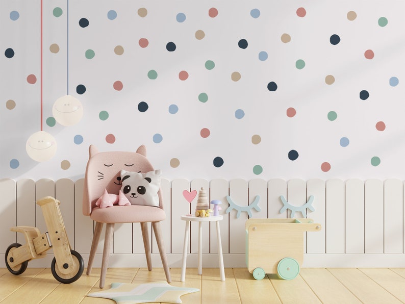 May include: A pink children's chair with a cat face design, a panda pillow, and a heart-shaped pillow. The chair is in a room with a white picket fence and a white wall with colorful polka dots. There are two hanging light fixtures with smiley faces.