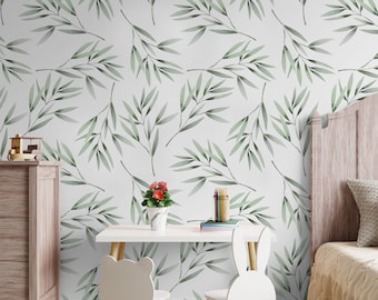 May include: A white wall with a green watercolor leaf pattern. A white desk with a white chair sits in front of the wall. A white bed with a beige blanket is in the background.