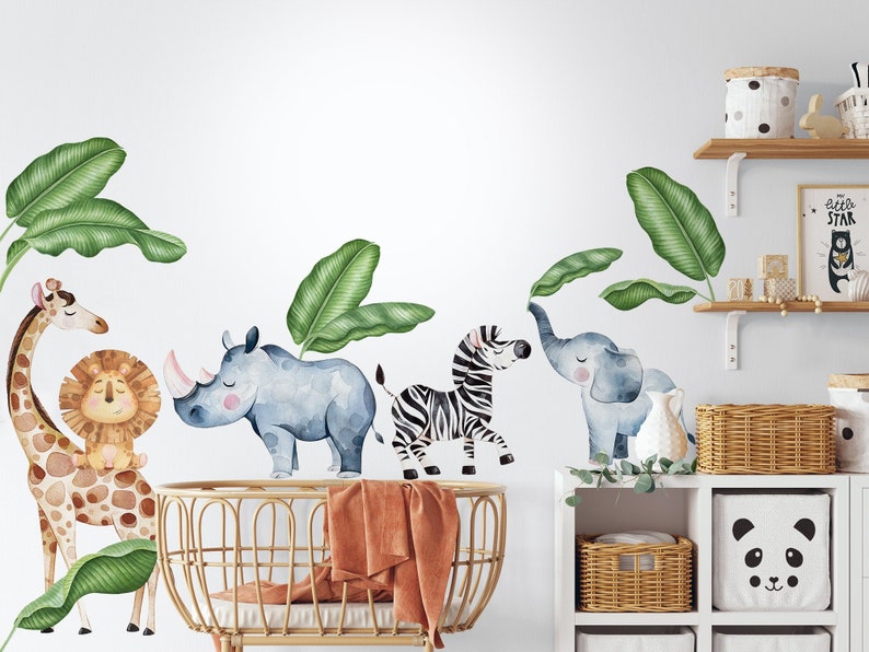 May include: A set of watercolour animal wall decals featuring a giraffe, lion, rhino, zebra, and elephant. The decals are surrounded by green banana leaf designs. The decals are shown on a white wall in a nursery setting.