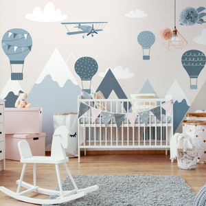 May include: A white crib with a blue and white patterned bunting hanging above it. The wall behind the crib is decorated with a mural of mountains, clouds, hot air balloons, and a plane. The room is decorated in a blue and white color scheme.