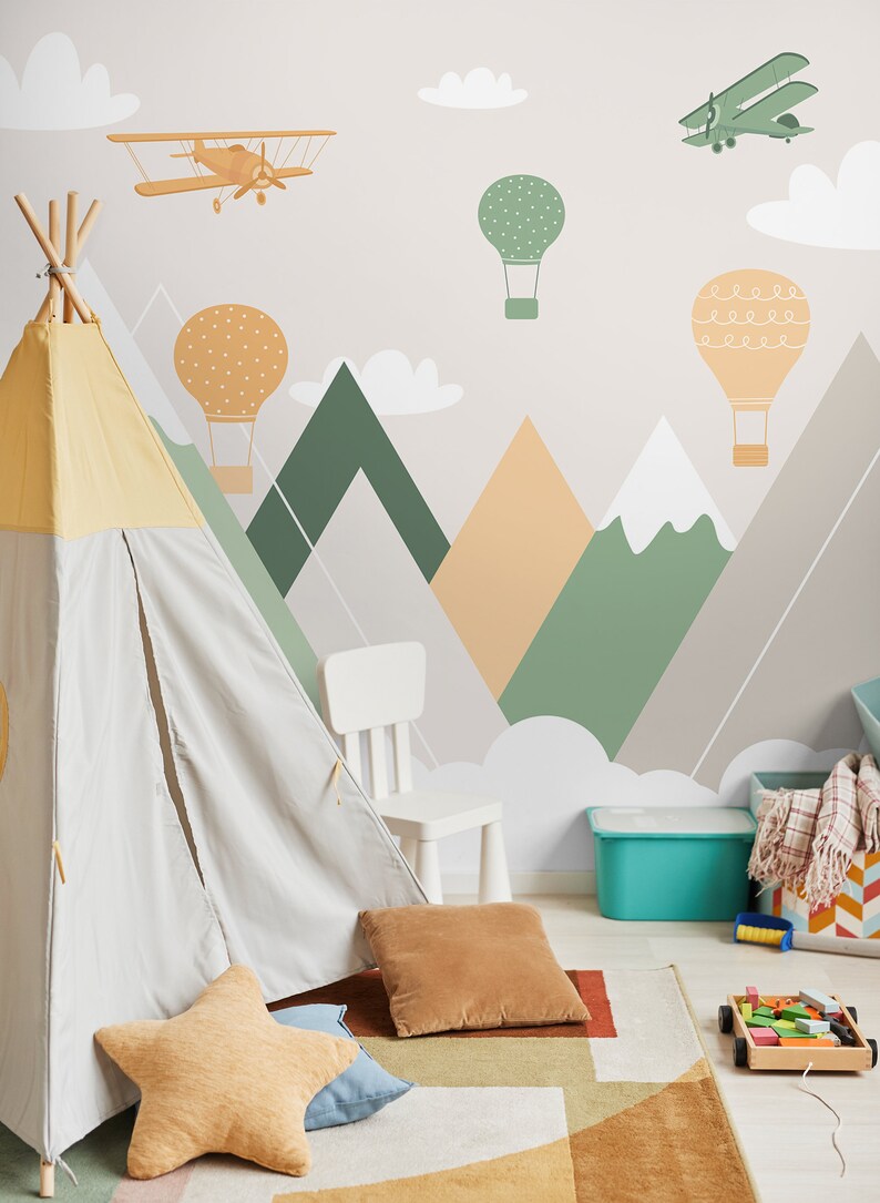 May include: A light gray teepee tent with a yellow top is set up in a playroom with a white chair and a blue storage bin. The wall is decorated with a mountain range mural with hot air balloons and airplanes.