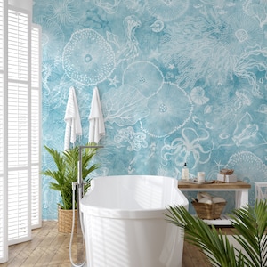 Könnte beinhalten: Eine weiße Badewanne steht in einem Badezimmer mit einer blauen und weißen Tapete mit Meeresmotiven. Die Tapete zeigt weiße Umrisse von Meeresbewohnern, Korallen und Muscheln auf hellblauem Hintergrund.