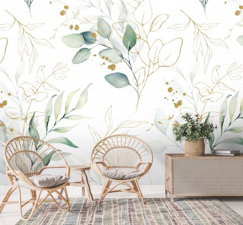 May include: Two wicker chairs with cushions sit in front of a wall with a green and gold floral wallpaper design. A wooden cabinet with a woven front sits in the background.