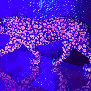 May include: A black and white jaguar figurine with pink and blue spots, illuminated under a black light.