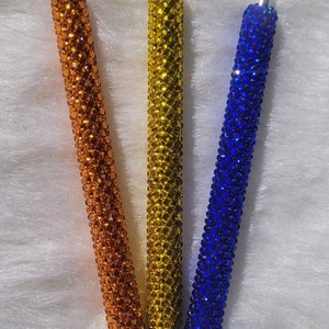 May include: Three pens with black tips and a sparkly finish. The pens are orange, yellow, and blue. The text "Orange", "Blue", and "Yellow" is written above each pen.
