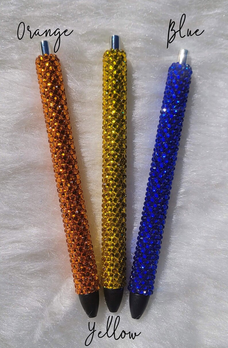 May include: Three pens with black tips and a sparkly finish. The pens are orange, yellow, and blue. The text "Orange", "Blue", and "Yellow" is written above each pen.