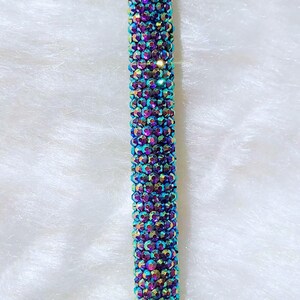 May include: A purple holographic pen covered in iridescent rhinestones. The pen is on a white fluffy surface. "Purple Holo" is written in black below the pen.