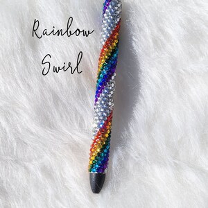May include: A rainbow swirl pen covered in colorful rhinestones. The pen is silver and has a black tip.
