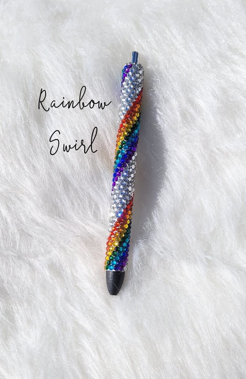 May include: A rainbow swirl pen covered in colorful rhinestones. The pen is silver and has a black tip.