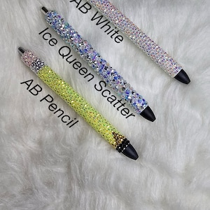 May include: Three rhinestone pens in different colors. The top pen is clear with iridescent rhinestones and the text "AB White". The middle pen is light blue with iridescent rhinestones and the text "Ice Queen Scatter". The bottom pen is yellow with iridescent rhinestones and the text "AB Pencil".