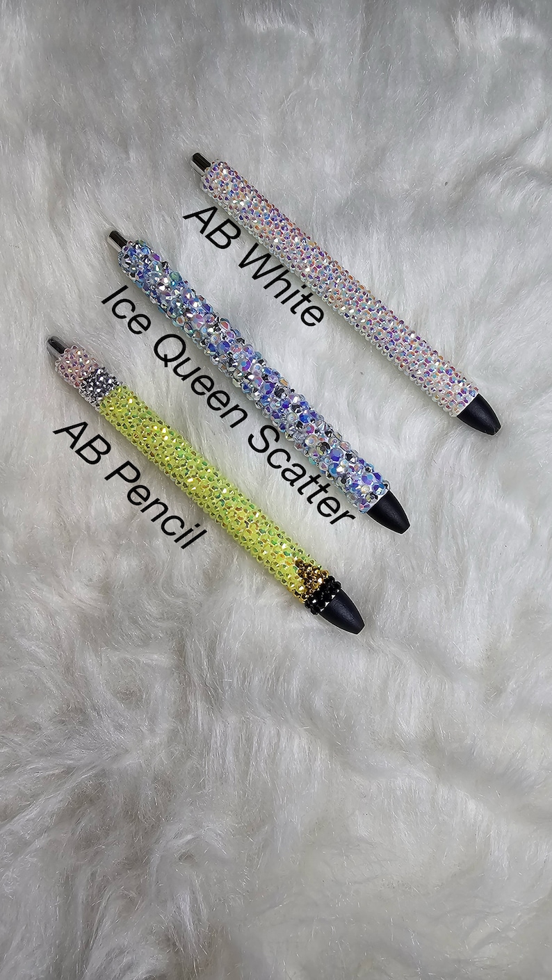 May include: Three rhinestone pens in different colors. The top pen is clear with iridescent rhinestones and the text "AB White". The middle pen is light blue with iridescent rhinestones and the text "Ice Queen Scatter". The bottom pen is yellow with iridescent rhinestones and the text "AB Pencil".