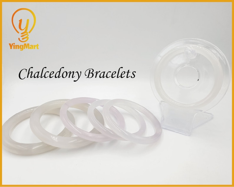 May include: Four white chalcedony bracelets of varying sizes, stacked on a white surface. The bracelets are smooth and polished, with a slight pink hue. The word "Chalcedony Bracelets" is written in black text above the bracelets.