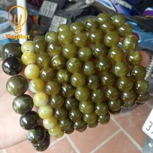 May include: A strand of green and yellow jade beads. The beads are round and smooth, and they are strung together on a clear string.