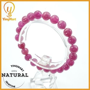 May include: A pink gemstone bracelet made of round beads. The bracelet is on a clear display stand. The text "Yingmart 100% NATURAL GEMSTONE" is on a white circle.