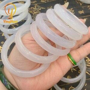 May include: A set of white jade bangles, stacked and displayed on a hand. The bangles are smooth and polished, with a subtle sheen.