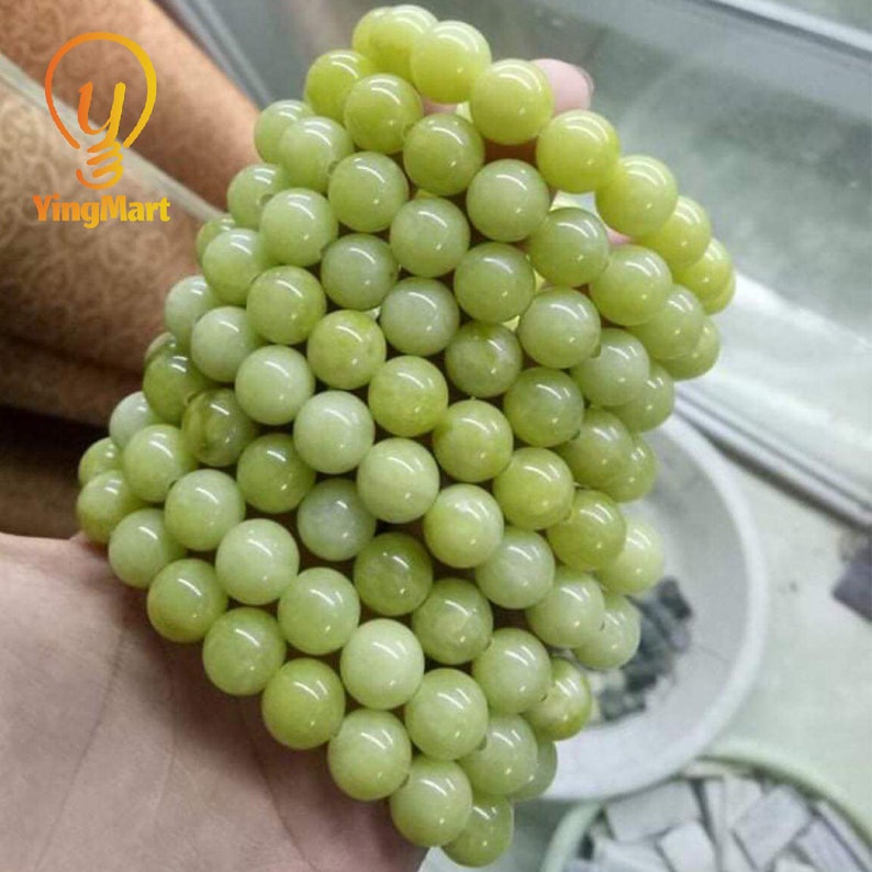 May include: A stack of light green jade beads, each bead is round and smooth. The beads are arranged in a circular pattern, creating a bracelet.