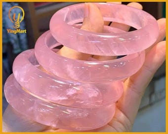 Pode incluir: Uma pilha de cinco pulseiras de quartzo rosa translúcido. As pulseiras lisas e polidas exibem uma cor rosa suave e uma textura de pedra natural. O logotipo YingMart é visível no canto superior esquerdo.