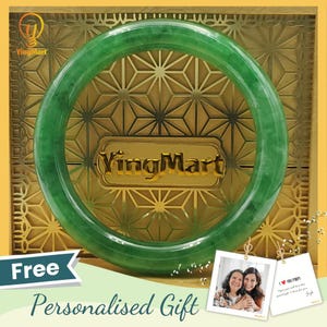 Puede incluir: Un brazalete de jade verde brillante. El brazalete circular se muestra sobre un fondo dorado con un diseño geométrico. El texto "YingMart" es visible. La imagen también incluye las palabras "Free" y "Personalised Gift".