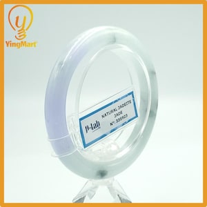 May include: A jadeite jade bangle bracelet, displayed on a clear acrylic stand. The bracelet has a pale lavender hue on one side, transitioning to a light green. A label reads "NATURAL JADEITE JADE".
