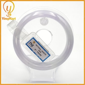 May include: A white jadeite bangle bracelet with a label that reads "PNJ NATURAL JADEITE JADE N°: 156099".