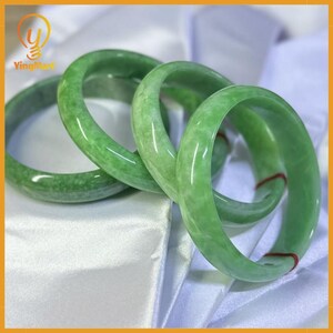 May include: Four green jade bangles are shown. The bangles have a smooth, polished finish and a circular shape. The jade appears translucent, with slight colour variations. The bangles are a type of jewellery.