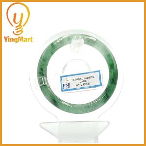 May include: A translucent green jadeite jade bangle bracelet. The bracelet is displayed on a clear stand, with a tag that reads "NATURAL JADEITE JADE N°: 242047". The jade has a mottled appearance with varying shades of green.
