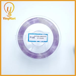 Puede incluir: Un brazalete de amatista púrpura translúcida se muestra en un recipiente de plástico transparente. El brazalete es una banda circular con diferentes tonos de púrpura. Una etiqueta dice "NATURAL AMETHYST" y "N°: 311243".