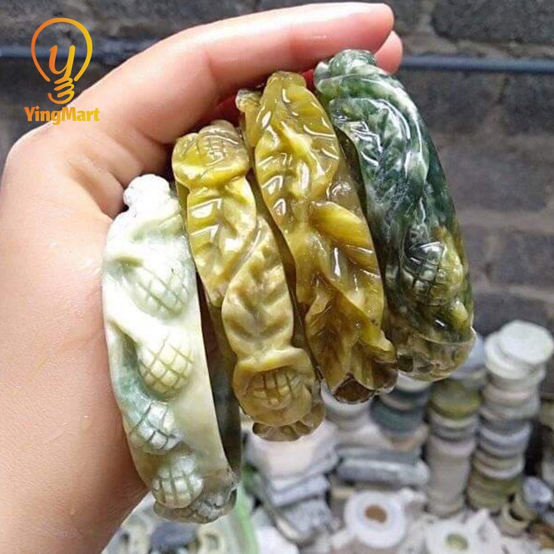 Pode incluir: Quatro pulseiras de jade esculpidas de forma intrincada em tons de verde e branco. As pulseiras apresentam um padr&atilde;o de folhas e est&atilde;o empilhadas umas sobre as outras.