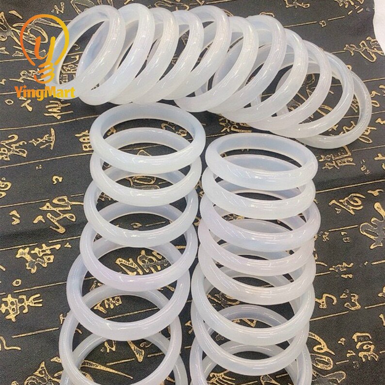 May include: A stack of white jade bangles, each with a smooth, polished finish. The bangles are arranged in a circular pattern, creating a visually appealing display.