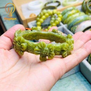 Pode incluir: Um bracelete de jade verde com um design floral esculpido. O bracelete &eacute; feito de jade liso e polido e apresenta detalhes intrincados.