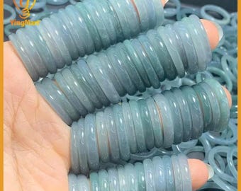 Pode incluir: Uma coleção de anéis de jade verde-claro. Os anéis são empilhados nos dedos, mostrando suas superfícies lisas e polidas. Os anéis têm uma qualidade translúcida, com variações sutis de cor. O fundo é preenchido com mais anéis de jade.